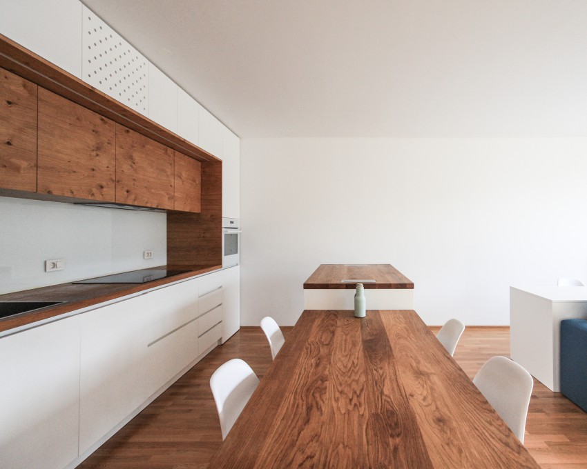 Kuhinja, ki je del odprtega bivalnega prostora, je izdelana po meri v beli barvi, dodani pa so poudarki v oljenem hrastovem lesu, z vidnimi grčami in manjšimi naravnimi nepravilnostmi. 