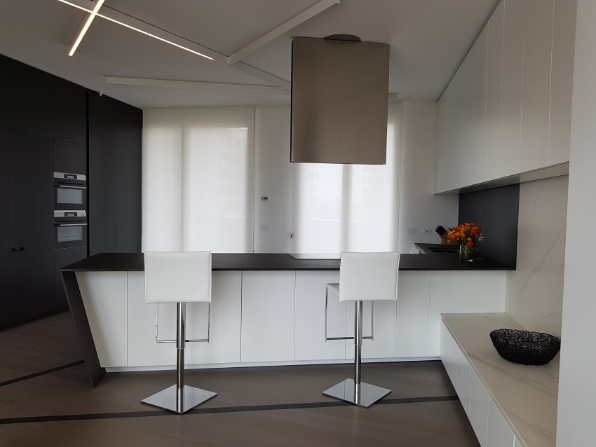 Kuhinja z visokimi omarami v črni in beli barvi brez ročajev deluje minimalistično s poudarjenimi arhitekturnimi linijami. 