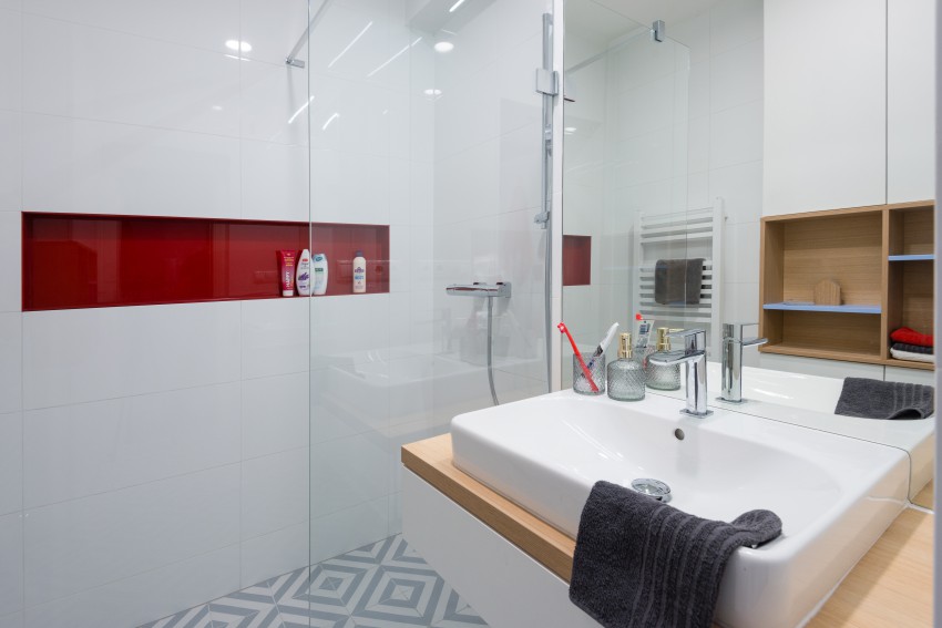  Če se v majhni kopalnici odločimo v glavnem za belo barvo, jo lahko na majhnih površinah popestrimo s kakšnim močnejšim odtenkom, kot je na fotografiji rdeča vzidana odlagalna polička v kabini za prhanje.