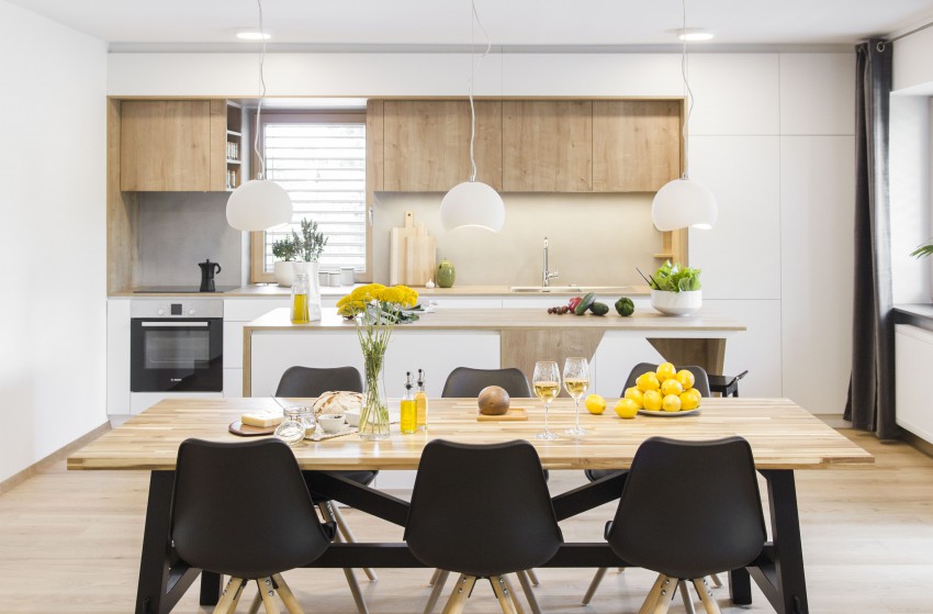Lesen vložek na belem pohištvenem ozadju se ponovi v kuhinji. Vanj je vizualno vključeno tudi okno z lesenim okvirjem, Poudarek belo-leseni kombinaciji dajejo temno sivi stoli in podnožje mize. 