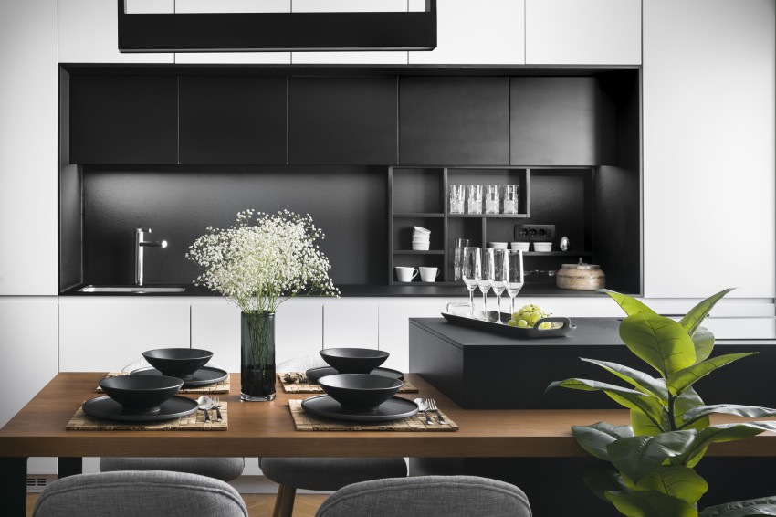 Kuhinja je odeta v bele in črne odtenke. Delovni otok v črni barvi preide v leseno jedilno mizo.