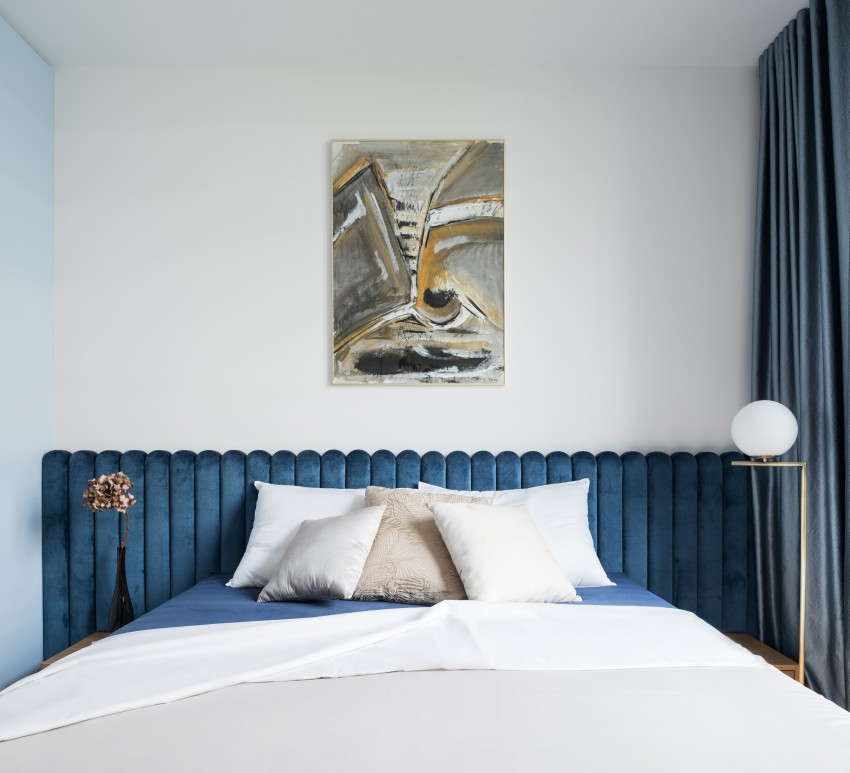 <p>Vzglavje postelje je oblečeno v zamolklo modri žamet, ki skupaj s skrbno izbranimi tkaninami v obliki zaves in blazin prostor naredijo bolj eleganten in prefinjen.</p>