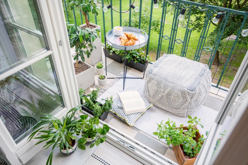 Poletni hygge na manjšem balkonu: udoben tabure ali počivalnik, klubska mizica in nekaj okrasnih rastlin.