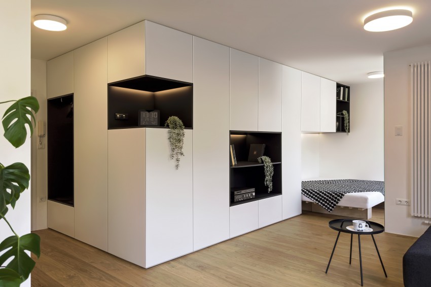 Interier zaznamuje mogočna omara, ki povezuje vse prostore stanovanja, zakrije inštalacijske jaške in manjše stene. Črni odprti kubusi naredijo iz nje vizualno atraktiven grafični element.